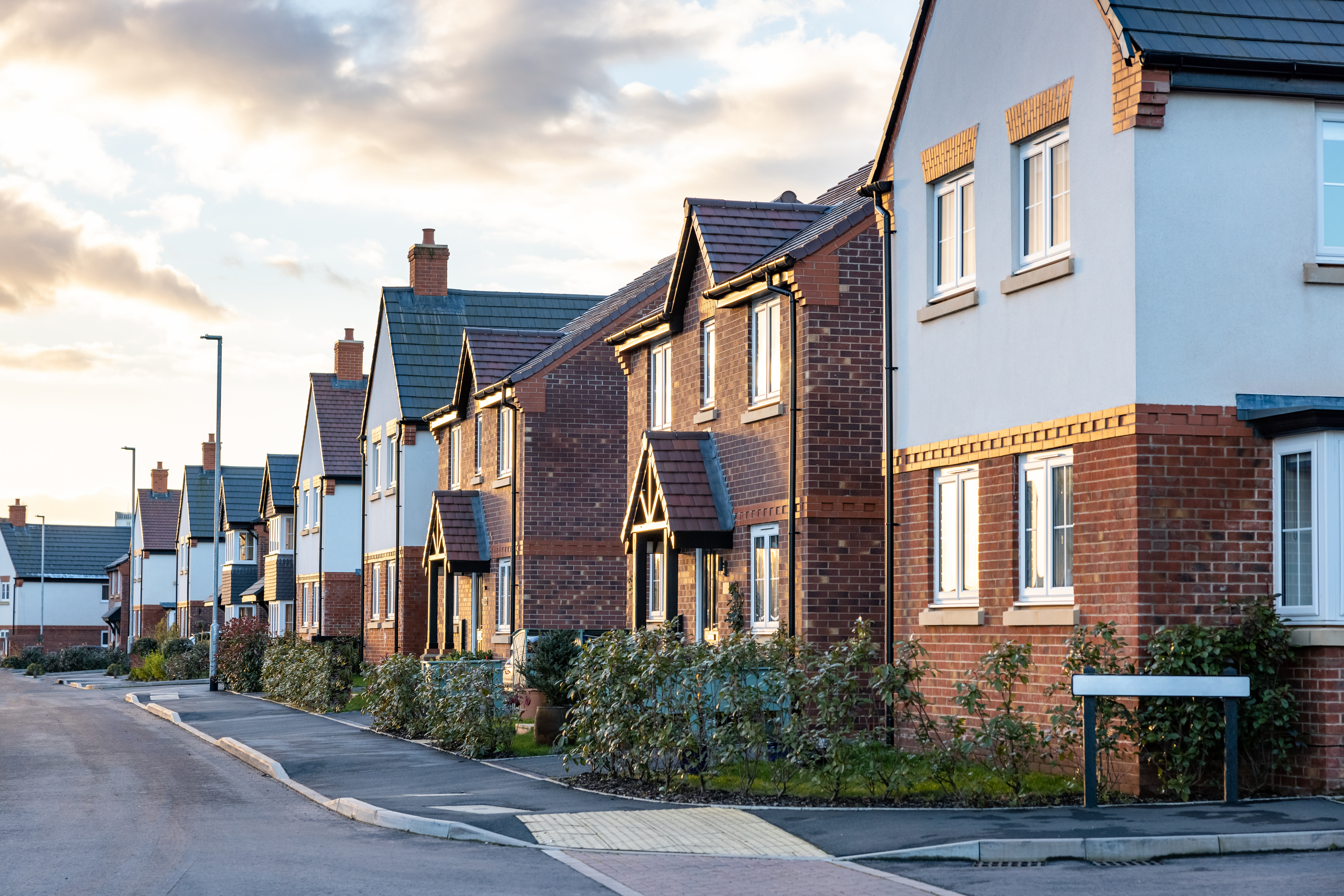 A quiet residential street with rows of houses under a cloudy sunset sky.